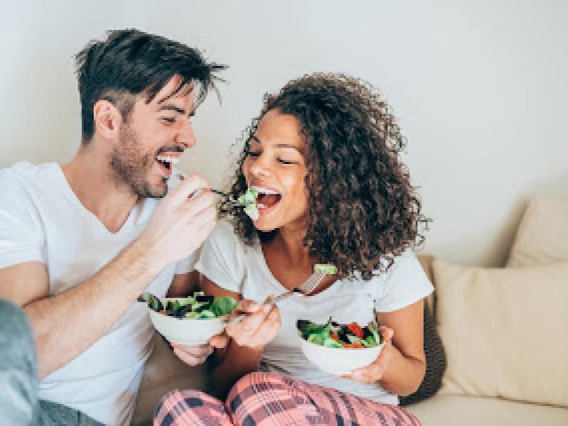 Happy man feeding his girlfriend with salad